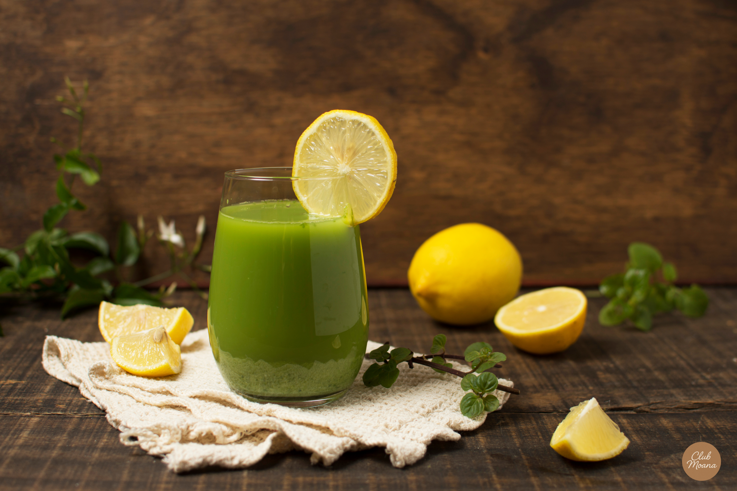 A vibrant green drink in a glass with lemon or herbs around it