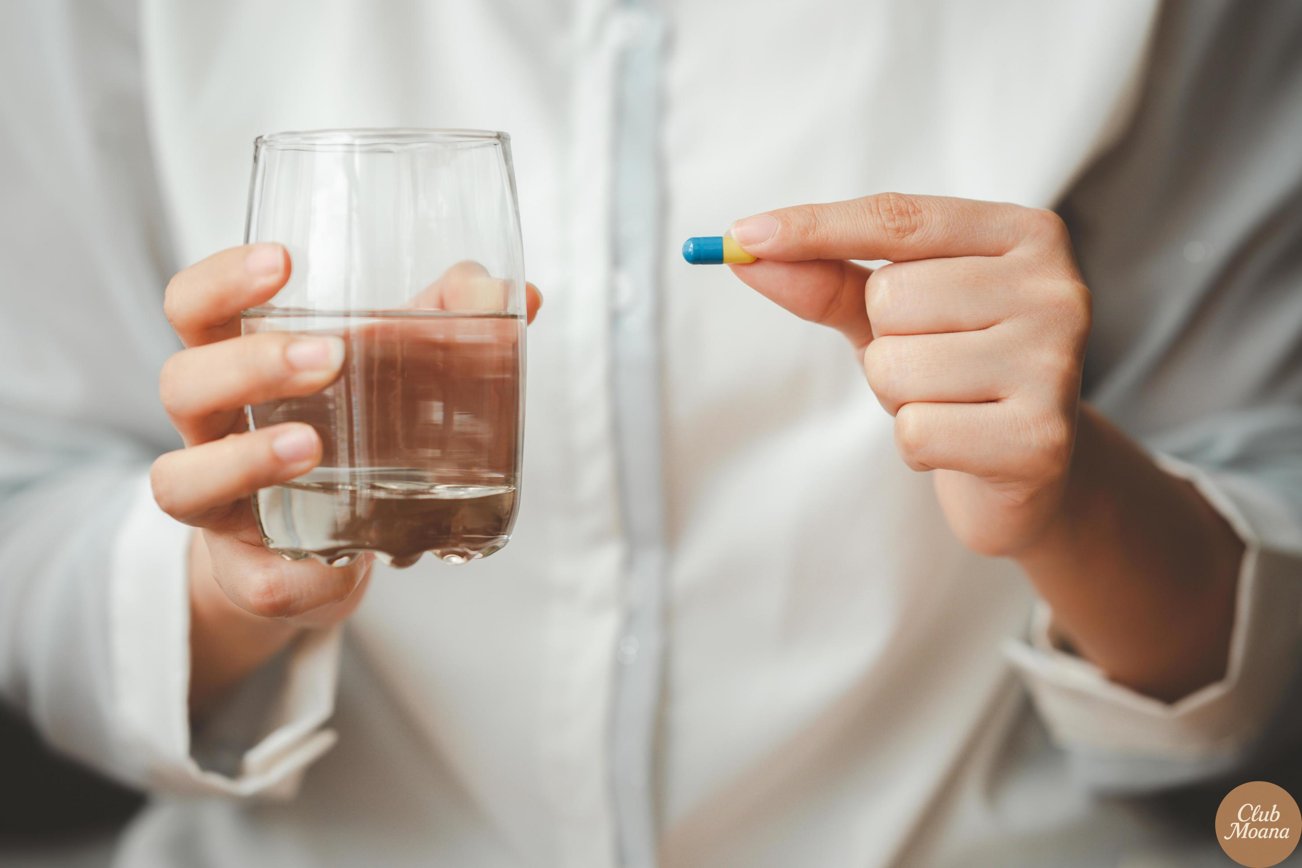 Hand holding 2 capsules next to water bottle